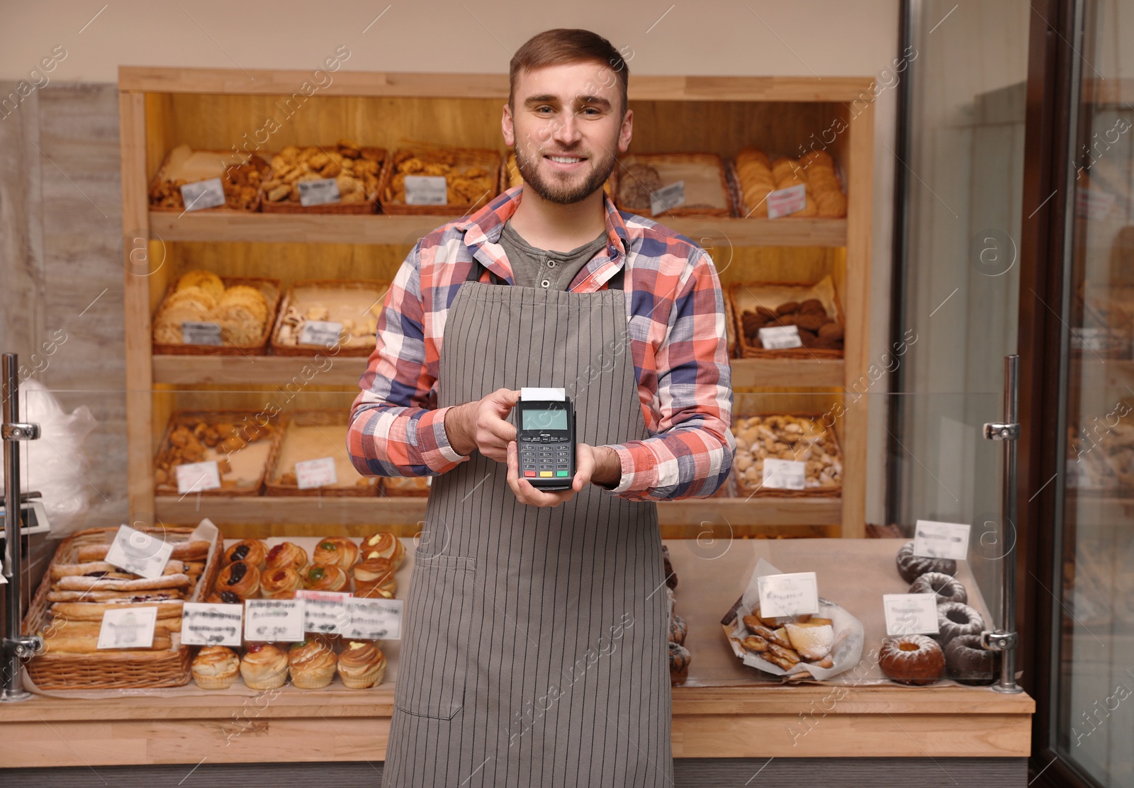 Photo of Smiling seller holding payment terminal in bakery