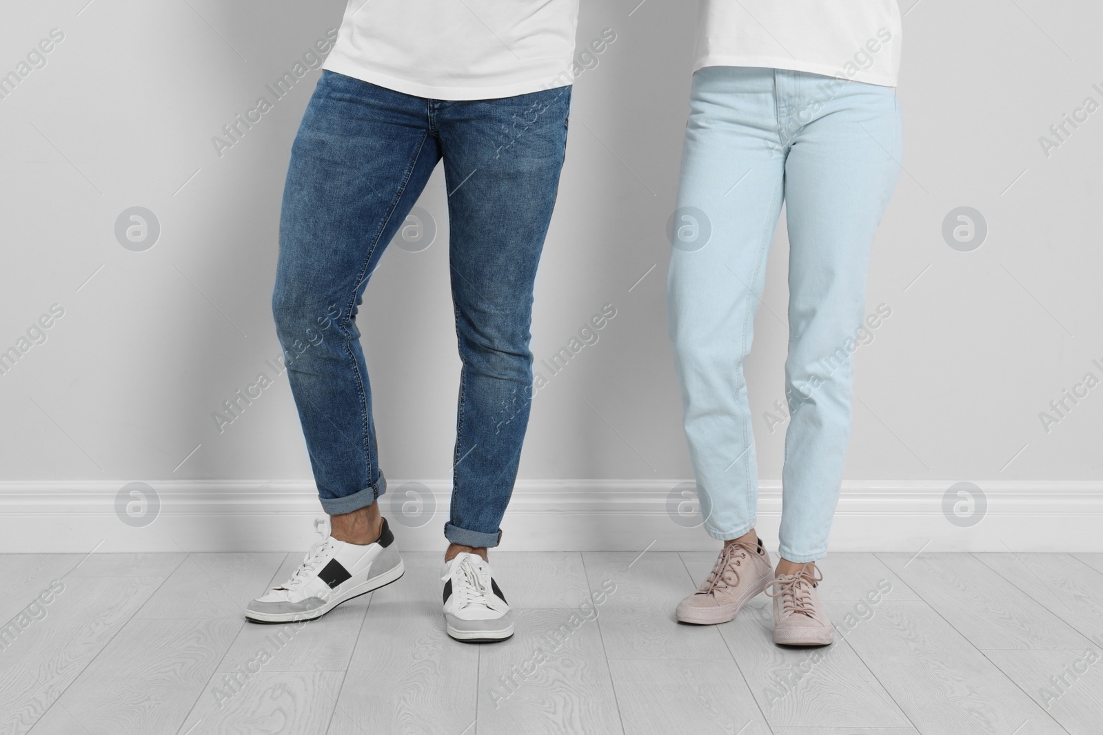 Photo of Young couple in stylish jeans near light wall, closeup