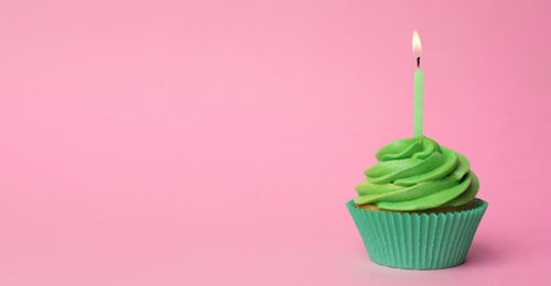 Delicious birthday cupcake with green cream and burning burning candle on pink background. Space for text