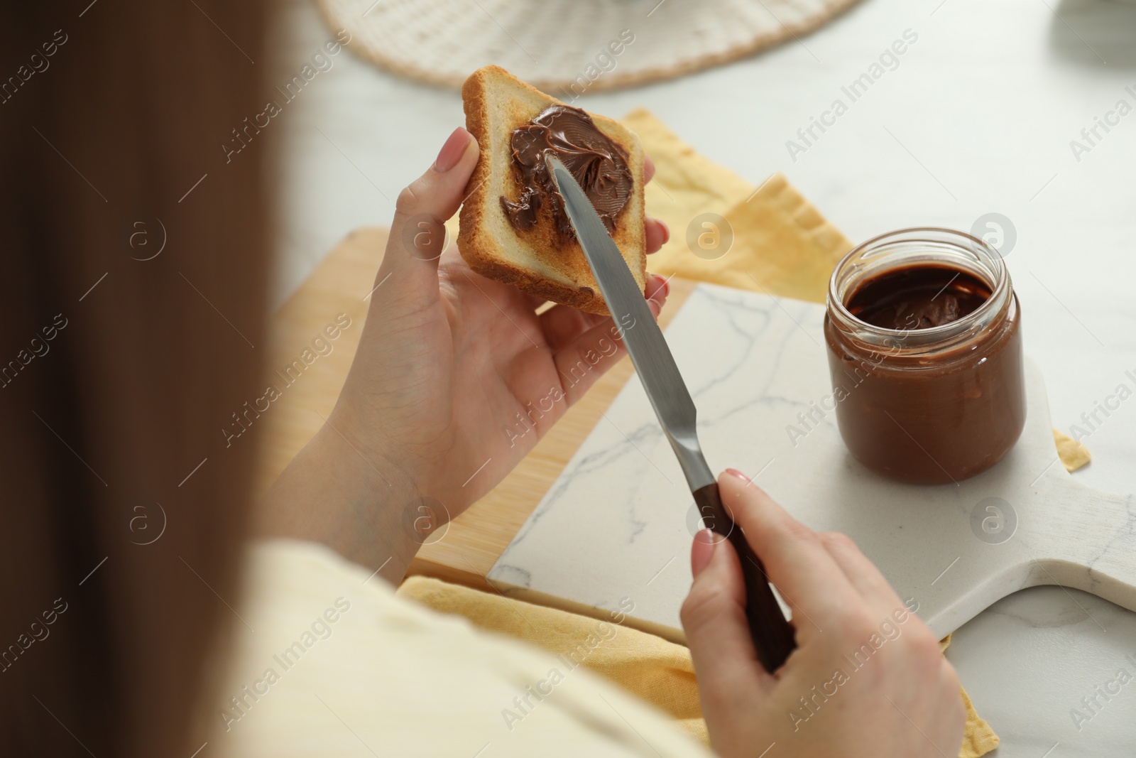 Photo of Woman spreading tasty nut butter onto toast at white table, closeup