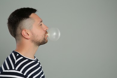 Handsome man blowing bubble gum on light grey background, space for text