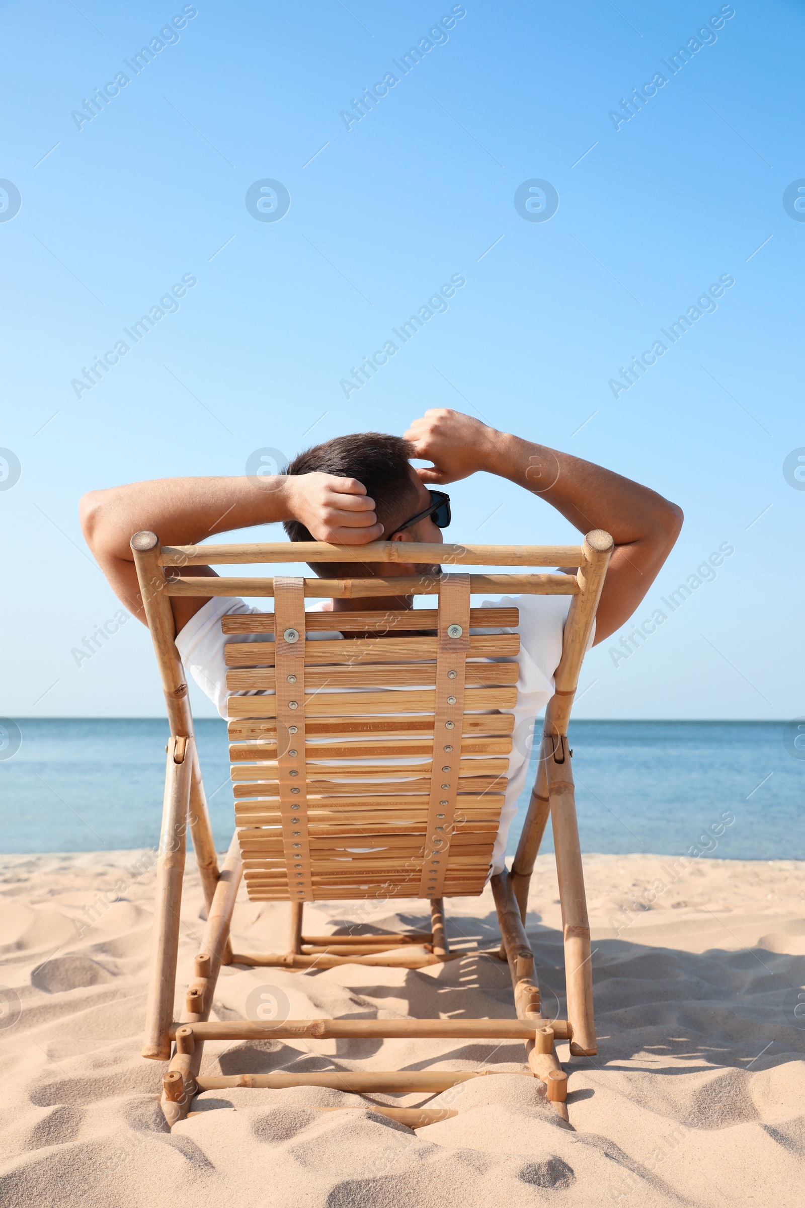 Photo of Young man relaxing in deck chair on sandy beach