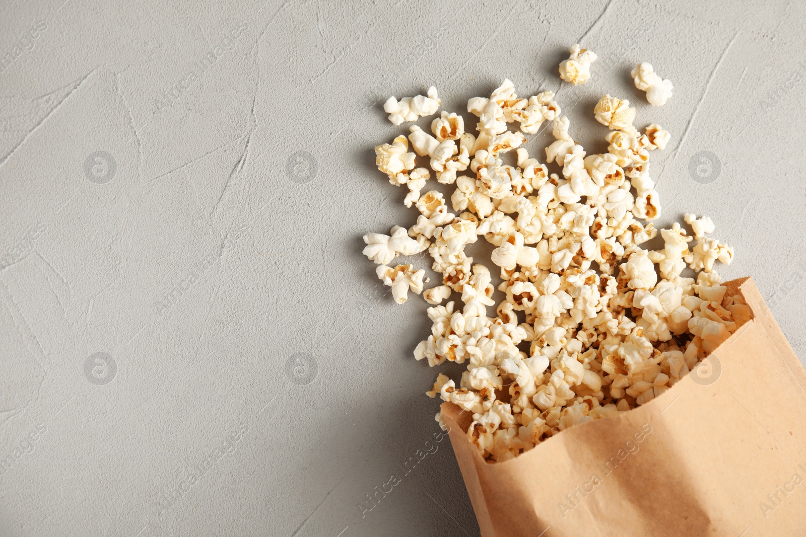 Photo of Paper bag with tasty popcorn on grey background, top view