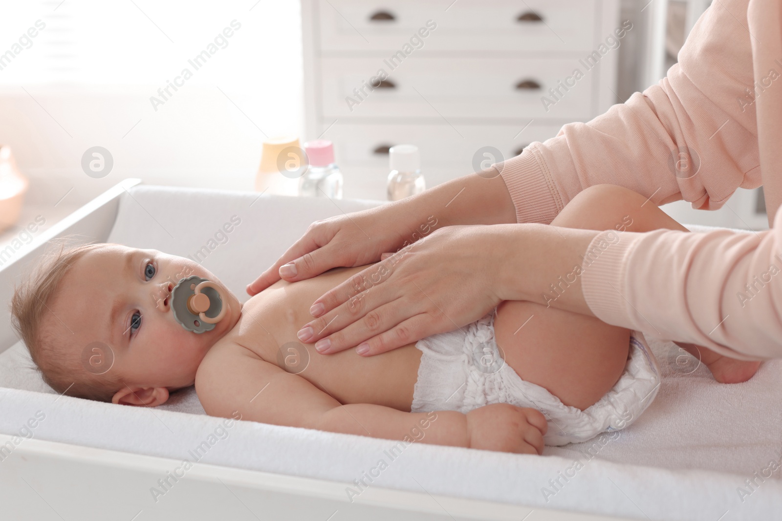 Photo of Mother massaging her cute baby with oil on changing table at home, closeup