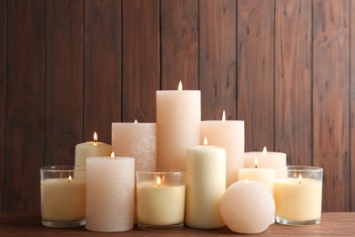 Photo of Set of burning candles on table against wooden background