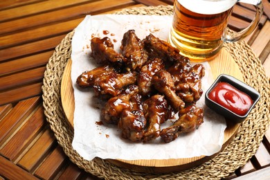 Photo of Tasty chicken wings, mug of beer and ketchup on wooden table. Delicious snack