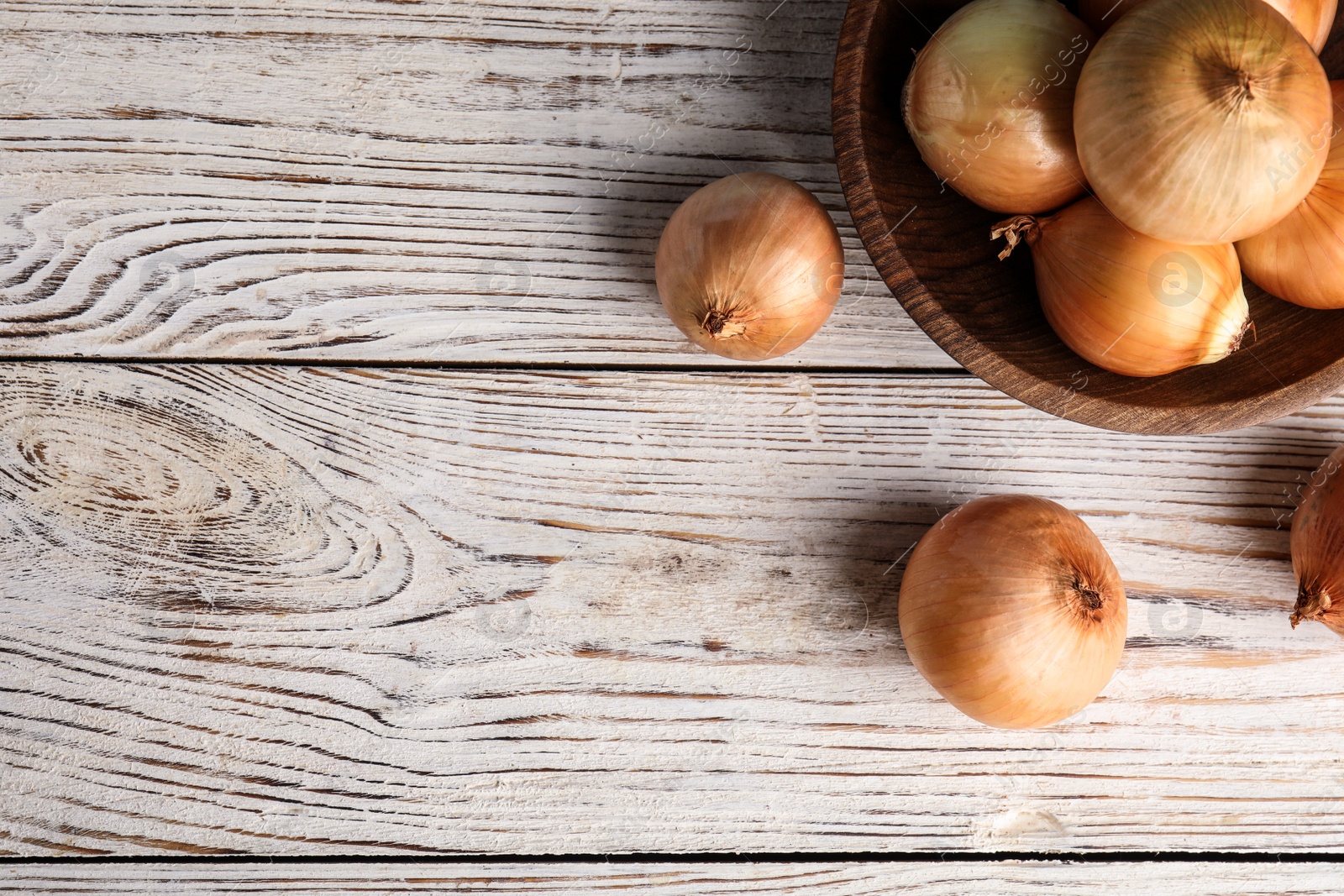 Photo of Bowl and ripe onions on white wooden table, flat lay. Space for text