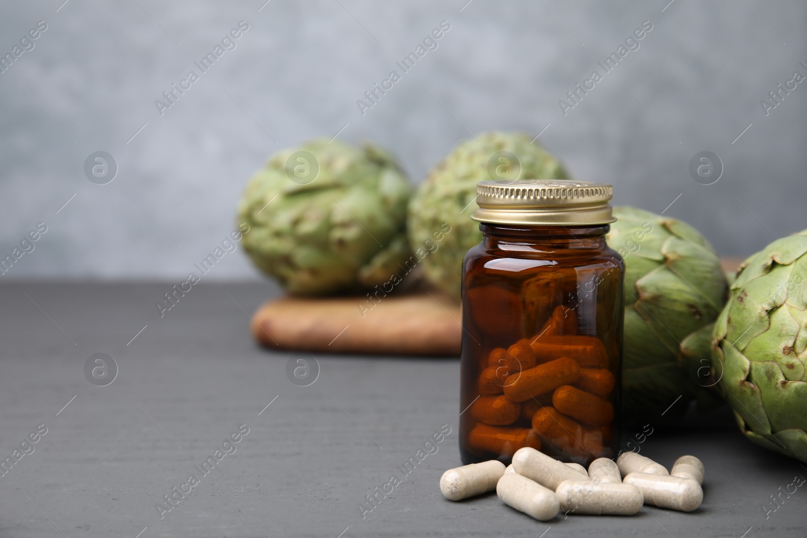 Photo of Bottle with pills and fresh artichokes on grey wooden table, closeup. Space for text