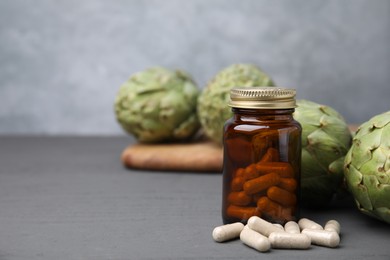 Bottle with pills and fresh artichokes on grey wooden table, closeup. Space for text