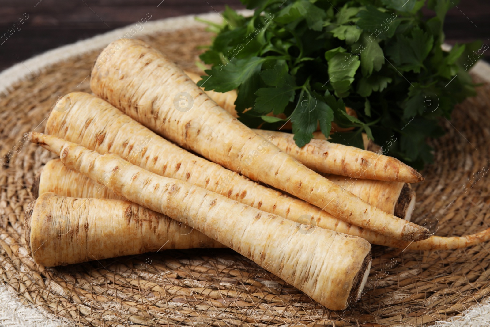 Photo of Raw parsley roots and fresh herb on wicker mat, closeup