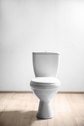 Photo of New ceramic toilet bowl near light wall
