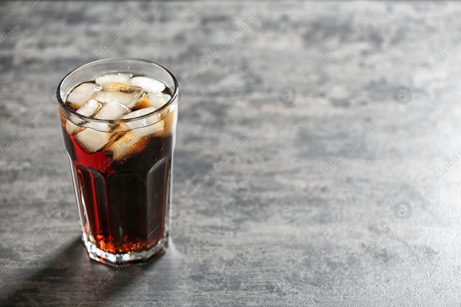 Photo of Glass of cold cola on grey table. Space for text