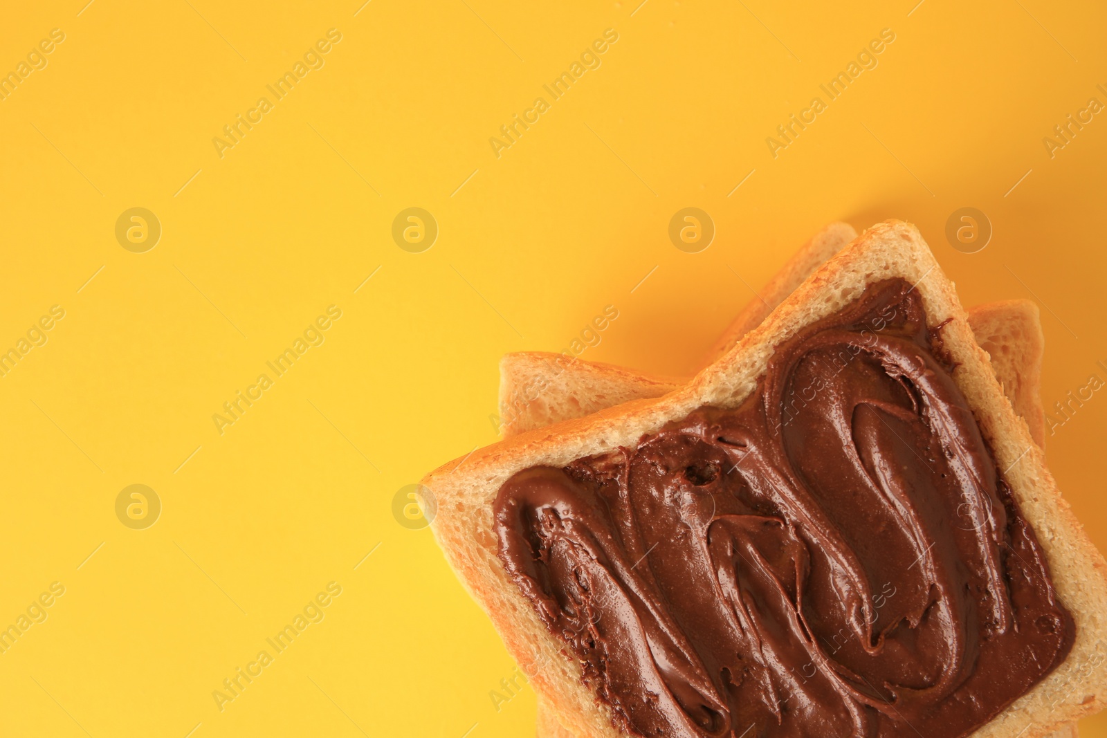 Photo of Tasty toast with chocolate paste on yellow background, top view. Space for text