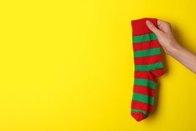 Photo of Woman holding striped sock on yellow background, closeup. Space for text