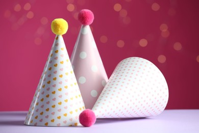 Photo of Party hats on violet table against pink background with blurred lights