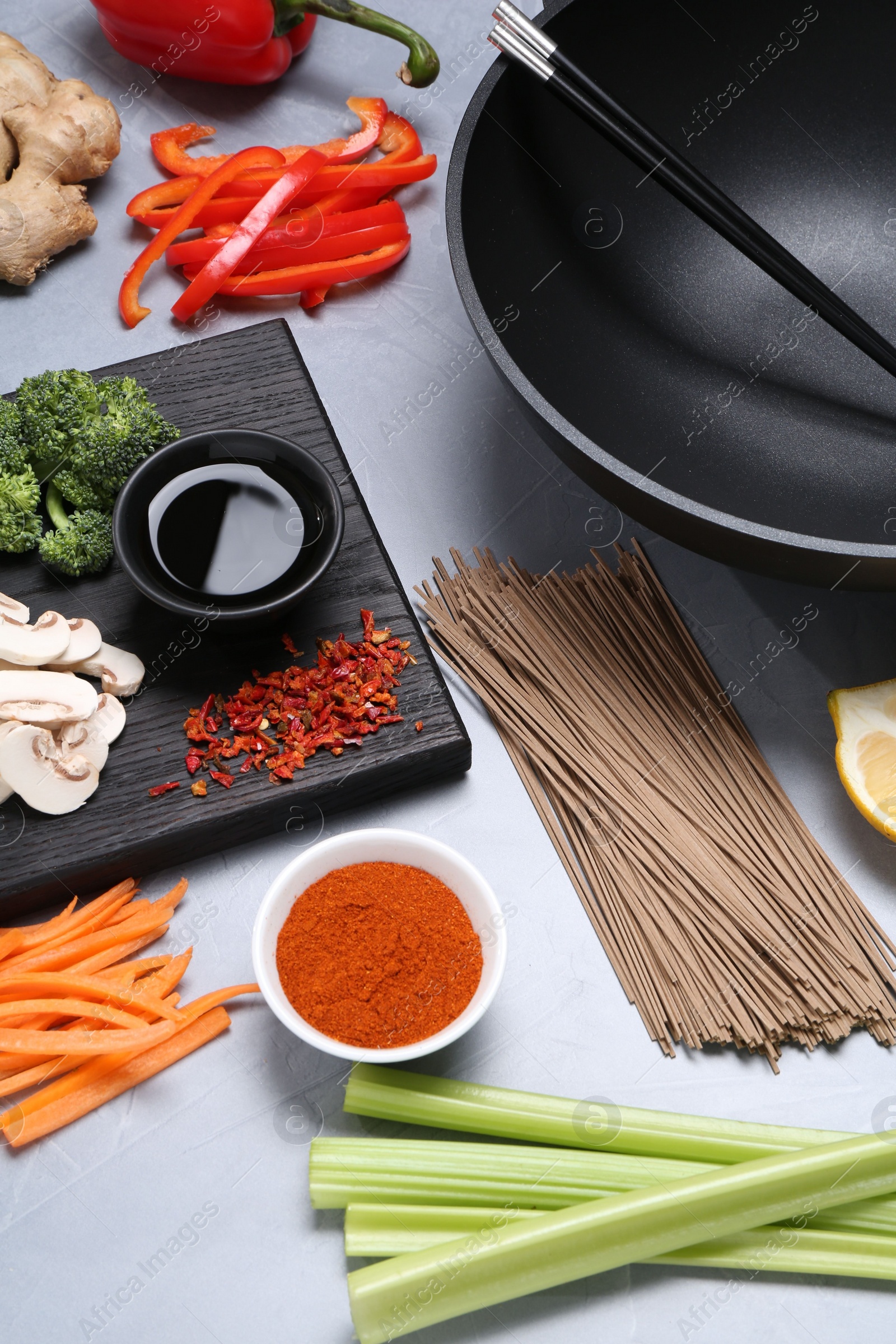 Photo of Wok, chopsticks and different products on grey table, closeup