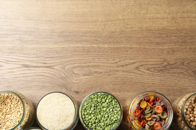 Photo of Glass jars with different products on wooden table, flat lay. Space for text