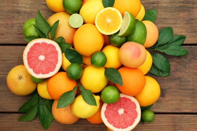 Photo of Different citrus fruits with green leaves on wooden table, flat lay