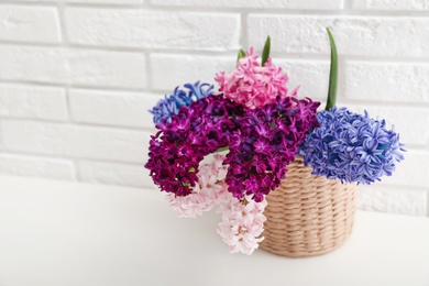 Photo of Beautiful hyacinths in wicker pot on table against brick wall, space for text. Spring flowers