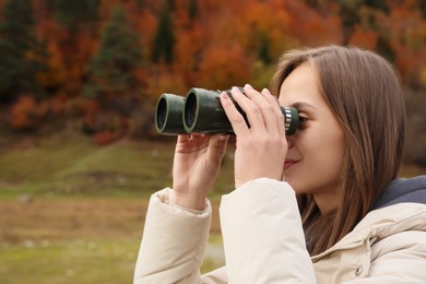 Photo of Woman looking through binoculars in beautiful mountains, closeup. Space for text