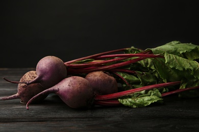 Photo of Fresh beets with leaves on dark wooden table against black background. Space for text
