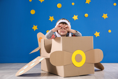 Photo of Cute little child playing with cardboard airplane near blue wall