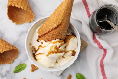 Photo of Scoopsice cream with caramel sauce, mint leaves and cone on white marble table, flat lay