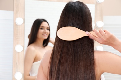 Beautiful young woman with hair brush looking into mirror in bathroom