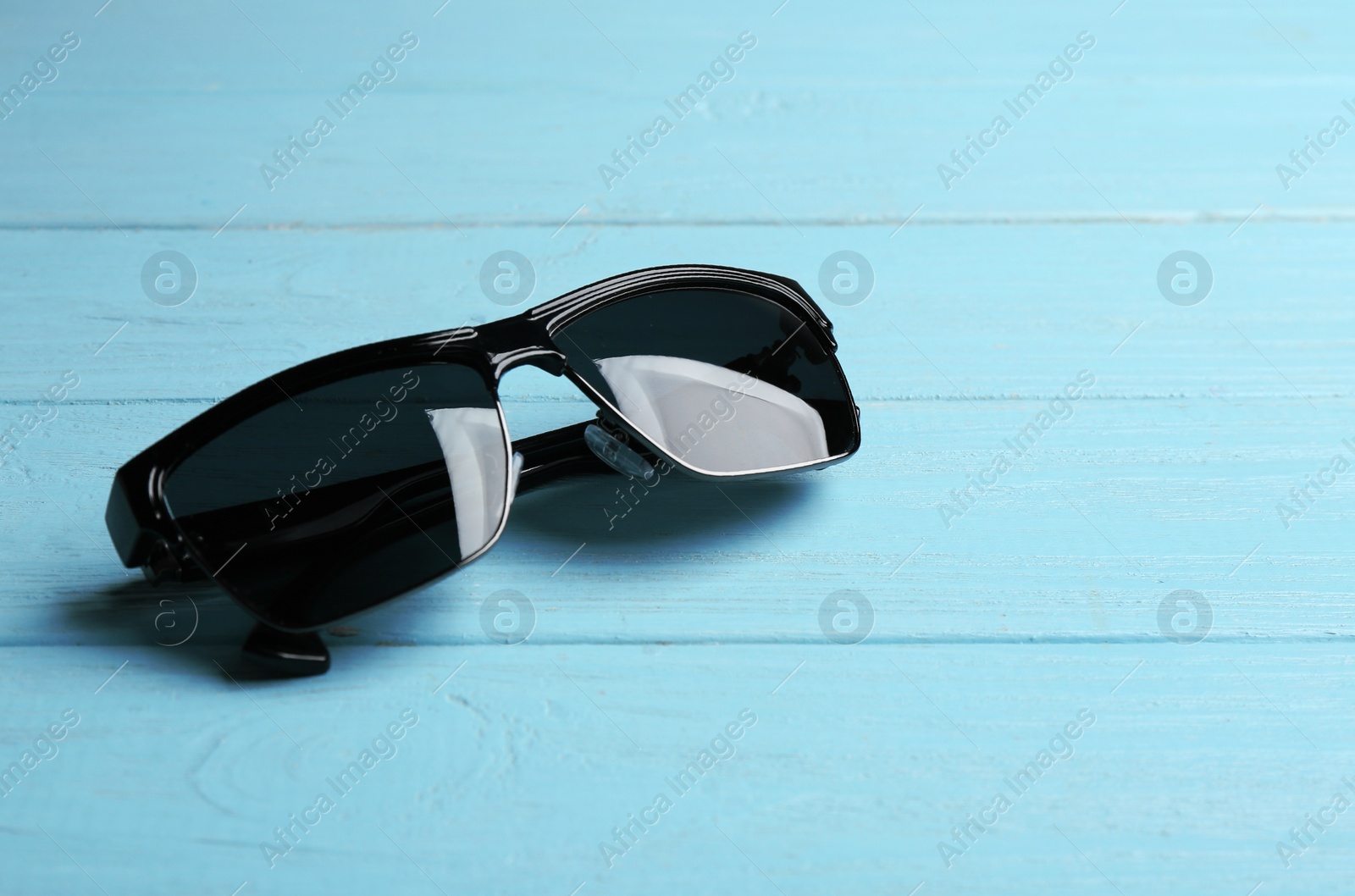 Photo of Stylish sunglasses on blue wooden background. Fashionable accessory