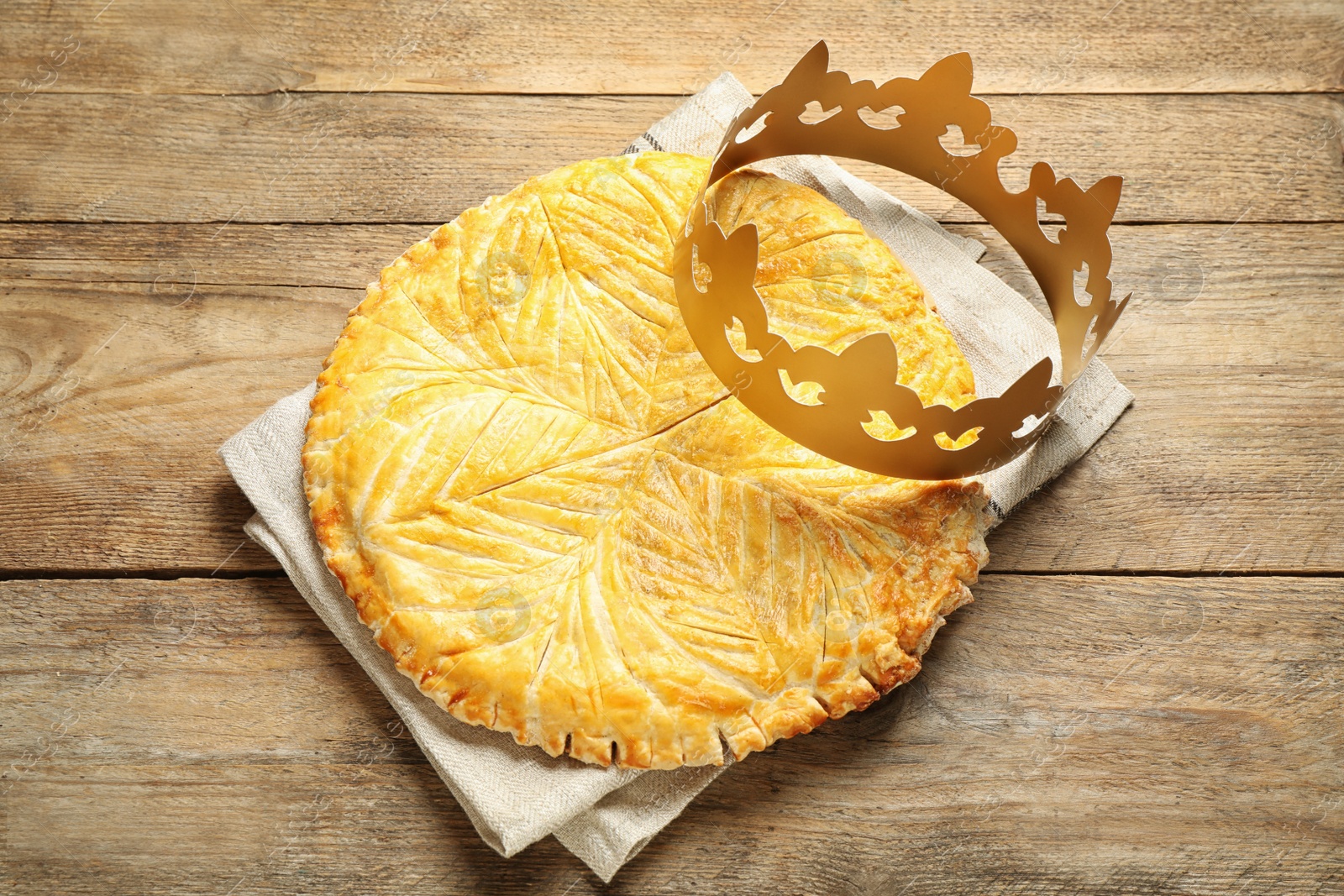 Photo of Traditional galette des Rois with paper crown on wooden table, flat lay