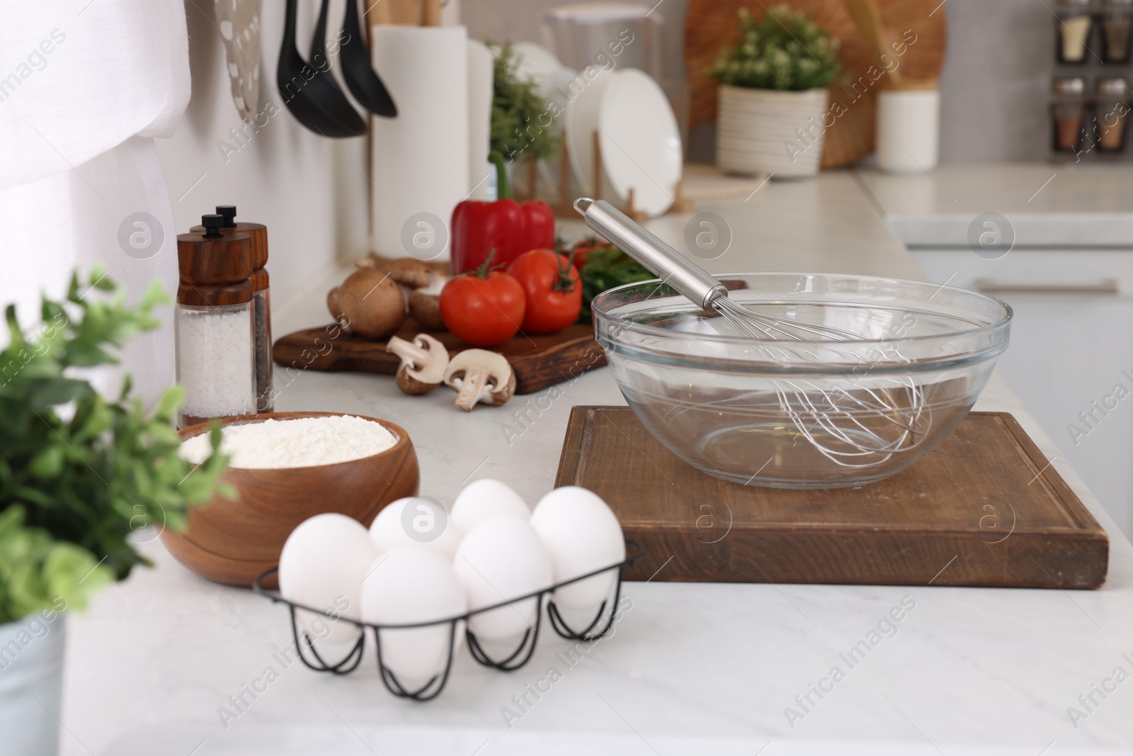 Photo of Metal whisk, bowl and different products on white table in kitchen