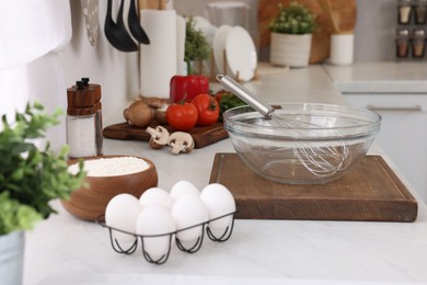 Photo of Metal whisk, bowl and different products on white table in kitchen