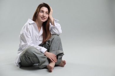 Portrait of beautiful young woman sitting on grey background, space for text