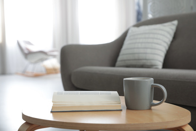 Photo of Book and cup of coffee on table near sofa. Interior design
