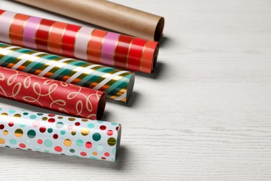 Photo of Different colorful wrapping paper rolls on white wooden table. Space for text