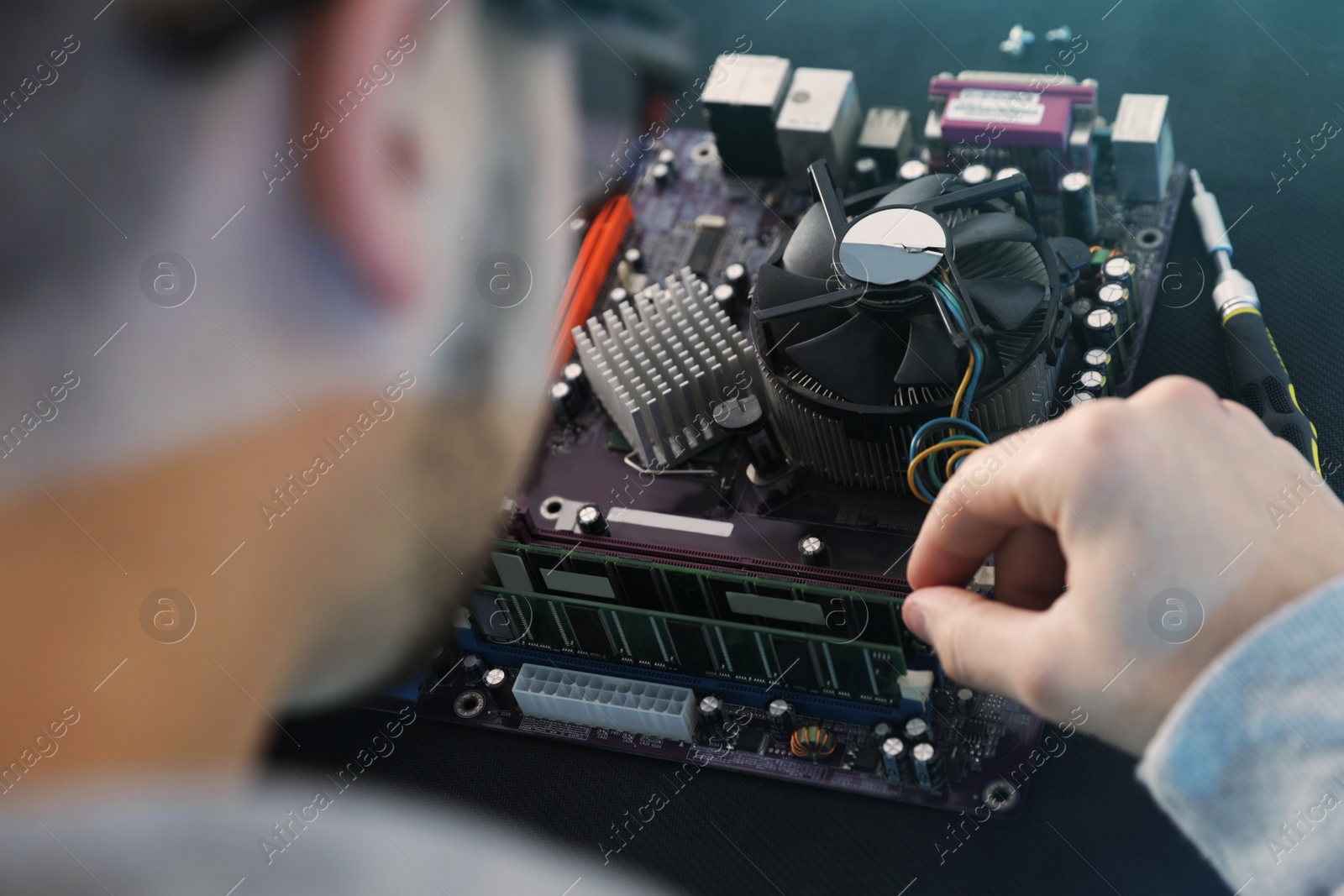 Photo of Male technician repairing motherboard at table, closeup