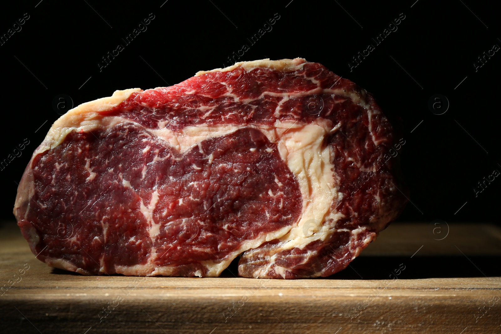 Photo of Piece of raw beef meat on wooden board against black background, closeup