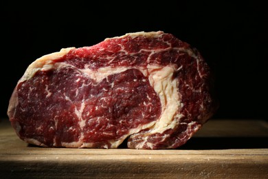 Photo of Piece of raw beef meat on wooden board against black background, closeup