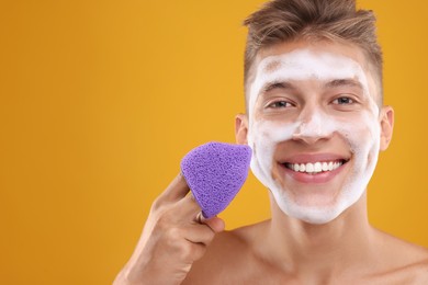 Photo of Happy young man washing his face with sponge on orange background. Space for text