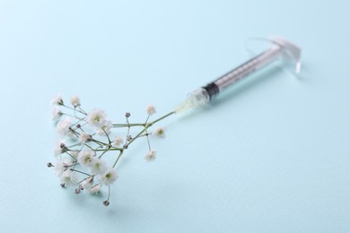 Photo of Cosmetology. Medical syringe and gypsophila on light blue background, closeup