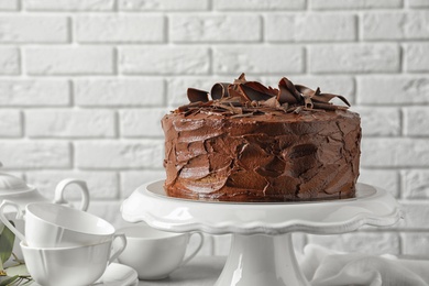 Stand with tasty homemade chocolate cake near white brick wall