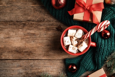 Photo of Cup of tasty cocoa with marshmallows, candy cane and Christmas decor on wooden table, flat lay. Space for text