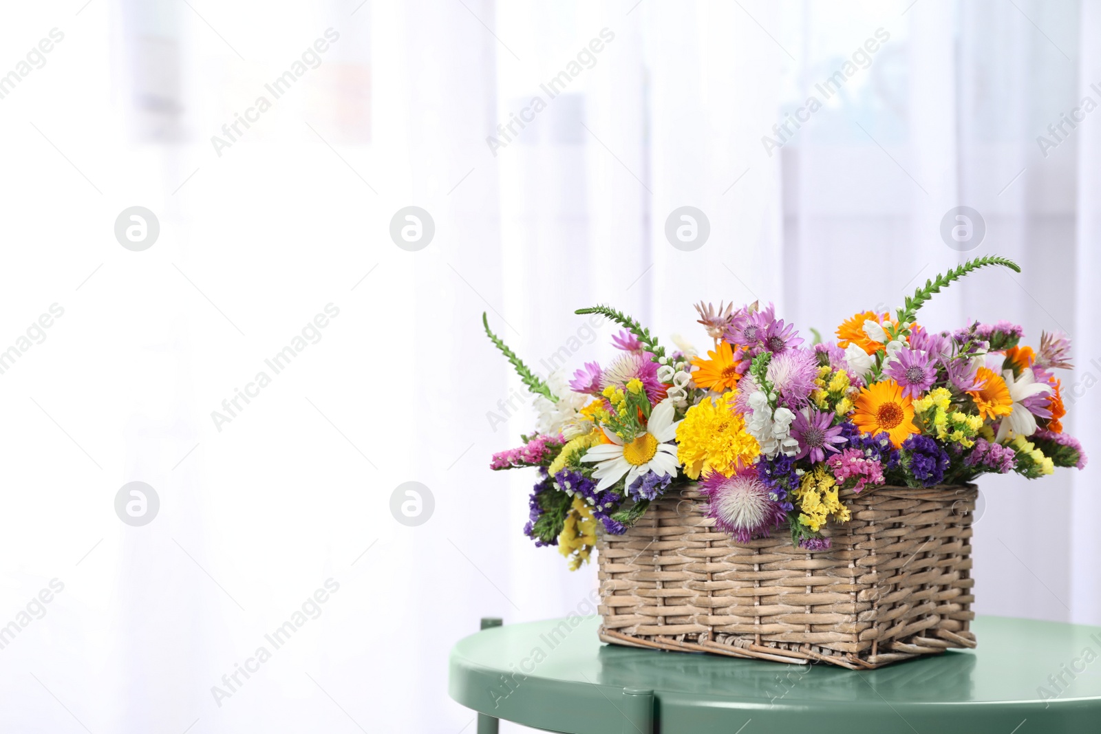 Photo of Wicker basket with beautiful wild flowers on table against light background