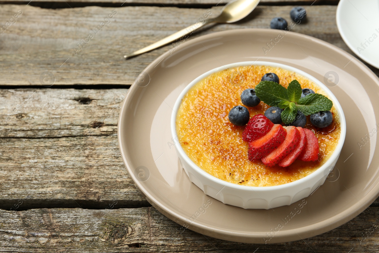 Photo of Delicious creme brulee with berries and mint in bowl on wooden table, closeup. Space for text