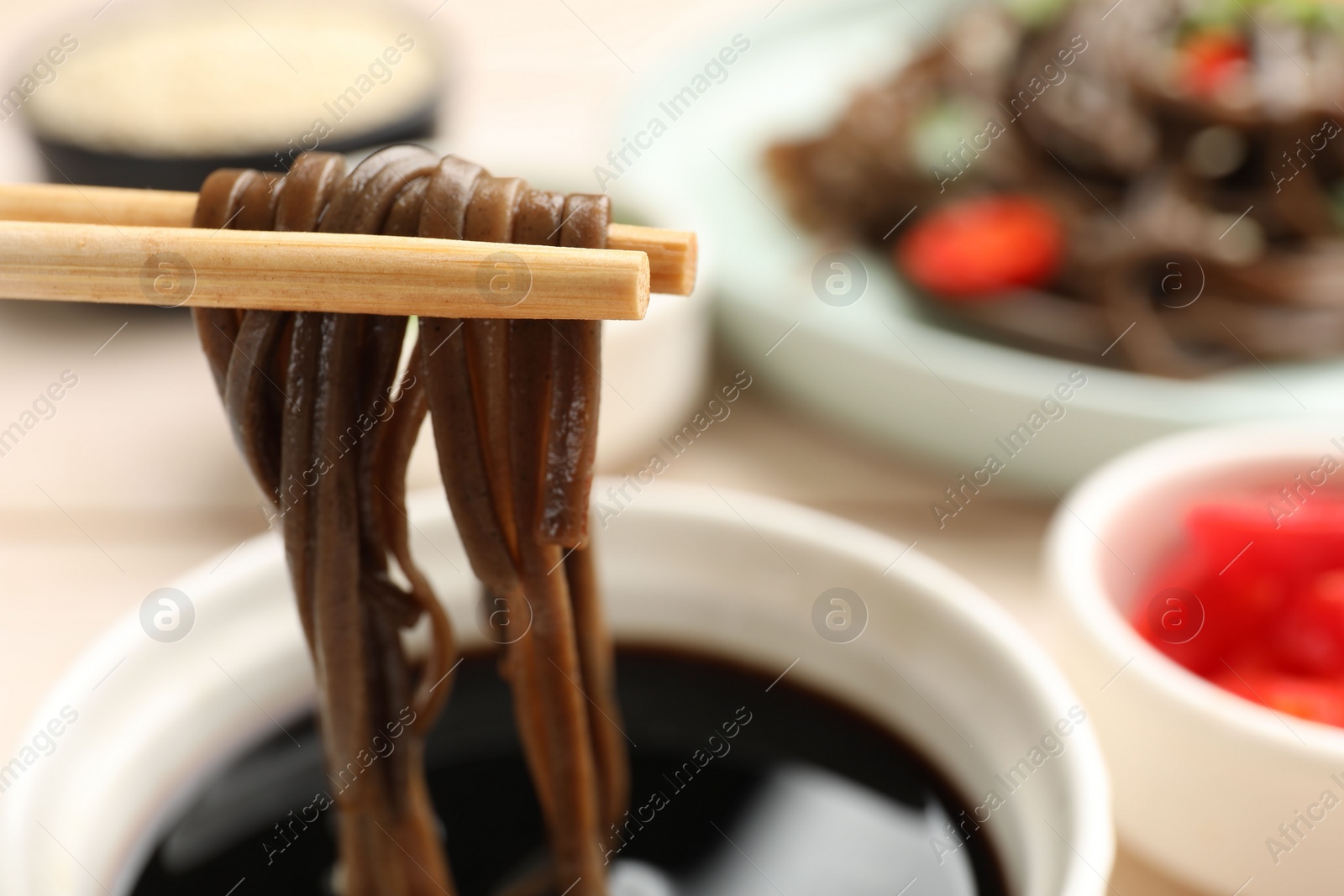 Photo of Eating delicious buckwheat noodles (soba) with chopsticks at table, closeup. Space for text