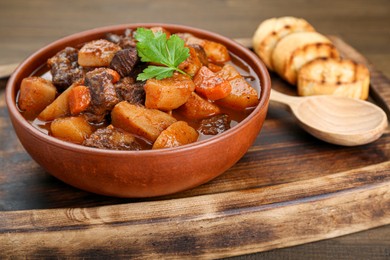 Photo of Delicious beef stew with carrots, parsley and potatoes served on wooden table, closeup