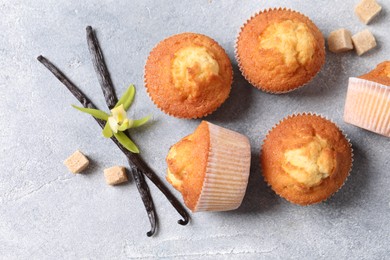 Photo of Delicious sweet muffins, vanilla pods and brown sugar on light grey textured table, flat lay