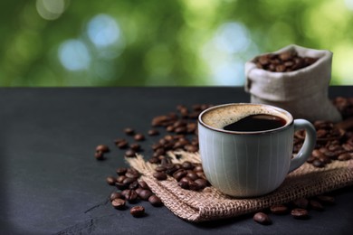 Cup of aromatic hot coffee and beans on black slate table outdoors. Space for text