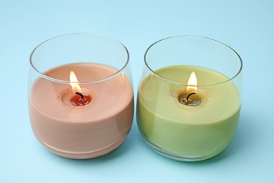 Photo of Burning wax candles in glass holders on light blue background