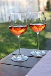 Photo of Glasses of rose wine on wooden table in garden